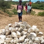 women hold rocks on head and throw in pile