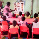 women in pink teach children sit on red table